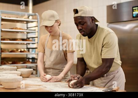 Black male and caucasian female bakers preparing dough for bread in bakery kitchen Stock Photo