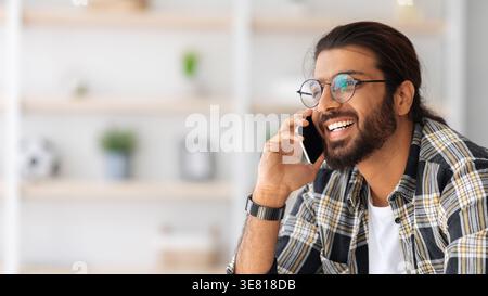 Arab man wearing eyeglasses having phone call looking away while sitting on sofa in living room at home Stock Photo