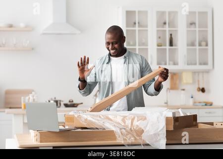 Black man holding wood waving at laptop during video call standing in kitchen at home Stock Photo