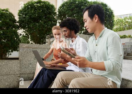 Diverse group of entrepreneurs having meeting using gadgets sitting on outdoor stairs during daytime Stock Photo