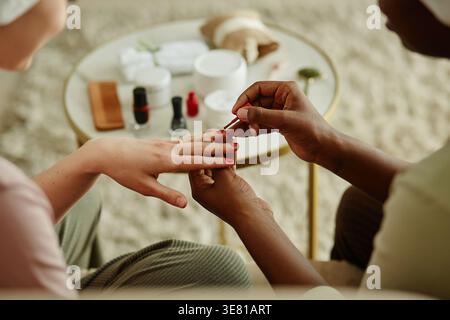 Black woman with towel on head doing manicure to female friend sitting together at home Stock Photo