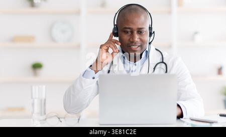 Black male doctor wearing headset talking to his patient while sitting at desk in clinic Stock Photo