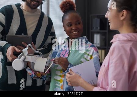 Group of diverse programmers discussing software and testing new VR glasses while standing together having a meeting in office Stock Photo
