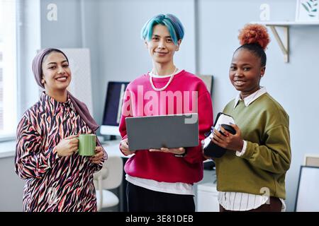 Group of programmers holding laptop and virtual reality headset while standing together in office Stock Photo