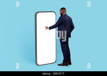 Black businessman in suit using smartphone while standing in front of blue background in studio Stock Photo