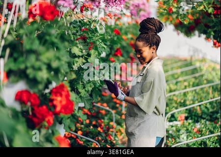 Black woman using tablet in checking flowers standing in greenhouse during daytime Stock Photo