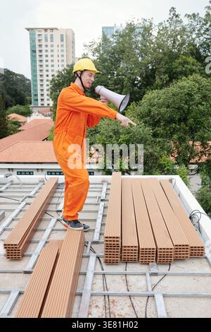 Mixed race male construction worker using megaphone looking away while standing in construction site Stock Photo