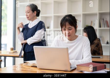 Asian college student working on laptop while listening to teacher giving lecture in classroom Stock Photo