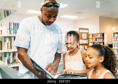 Black father reading a book while standing with daughters in the library Stock Photo