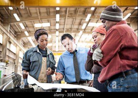Hispanic male manager discussing plans to team of workers standing in factory Stock Photo