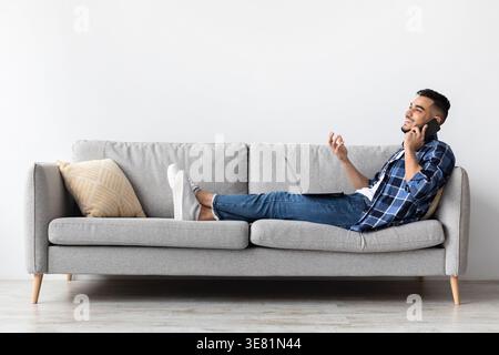 Middle Eastern man looking away having phone conversation sitting on sofa in living room at home Stock Photo