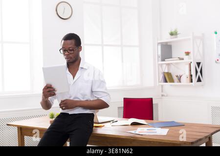 Black man wearing eyeglasses having video call on tablet sitting on table with papers in office Stock Photo