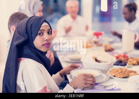 Serious Black woman with family and friends praying before having dinner sitting at table at home Stock Photo