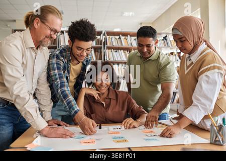 Diverse group of students studying together with male teacher in library Stock Photo