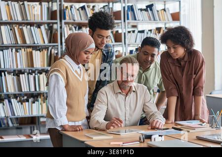 Group of students looking at tablet having lesson with male teacher in library Stock Photo
