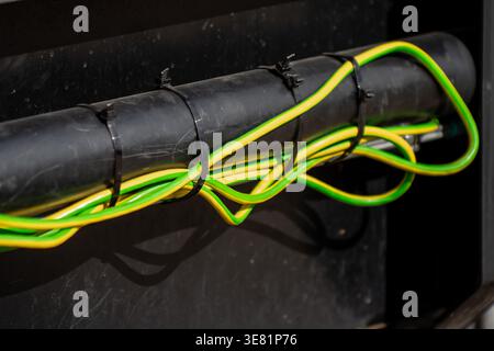 Close up of yellow and green electrical grounding wires secured to a black plastic protective pipe with plastic zip ties on industrial machinery or bu Stock Photo