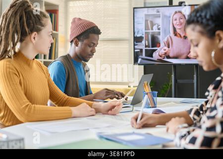 Group of students having online lesson with caucasian woman while sitting at table in class Stock Photo