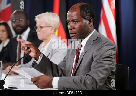 Black middle-aged male politician holding document pointing finger away giving his speech while sitting at table with diverse colleagues during pre... Stock Photo