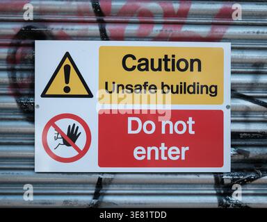 Yellow And Red Caution Sign On A Metal Roller Shutter Warning Of An Unsafe Building And Prohibiting Entry Stock Photo