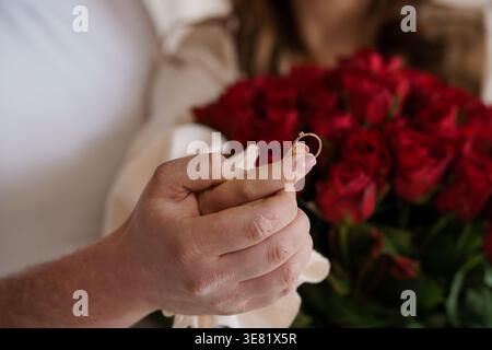 Close up of a hand presenting a sparkling diamond ring against a lush red floral background Stock Photo