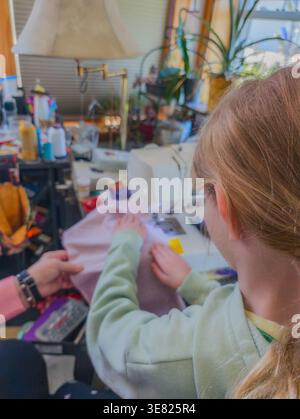 Child learns sewing skills with assistance in a busy home workshop during daylight hours Stock Photo