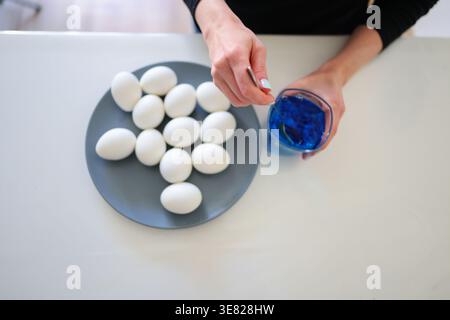 White eggs on plate and blue dye, process of coloring eggs for Easter celebration. Stock Photo