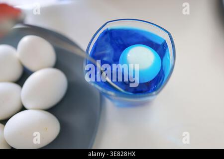Hands dyeing eggs in blue liquid, Easter decoration and creative family activity. Stock Photo