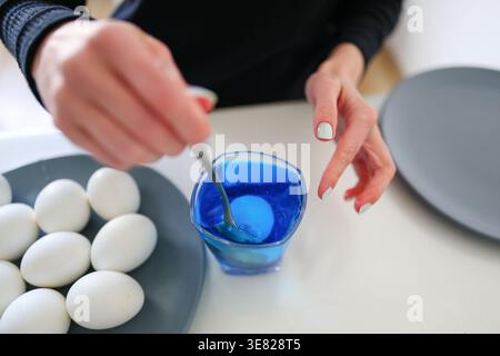 Blue dye solution with egg inside, process of coloring eggs for Easter holiday. Stock Photo