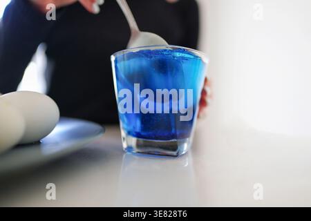 Close-up of egg dyeing in blue liquid, Easter preparation and creative home activity. Stock Photo