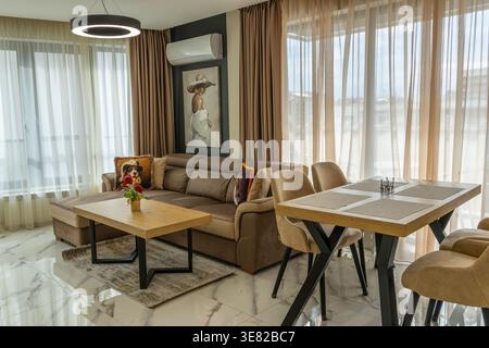 Bright modern apartment with marble flooring. Features a velvet sofa, wood tables, and a chic chandelier. Perfect example of contemporary open-plan Stock Photo