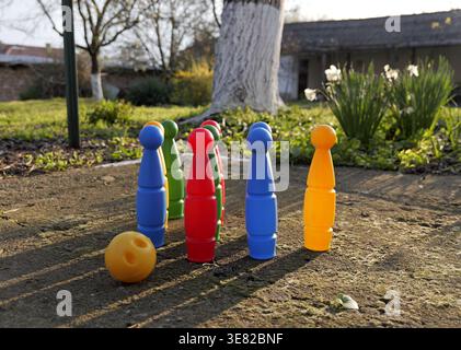 Colorful plastic bowling pins arranged in a triangle on a rough concrete surface outdoors, with strong sunlight casting long shadows in a garden. 2026 Stock Photo