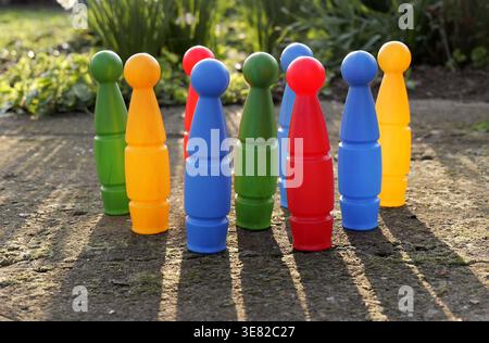 Colorful plastic bowling pins arranged in a triangle on a rough concrete surface outdoors, with strong sunlight casting long shadows in a garden. 2026 Stock Photo