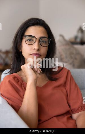 Thoughtful woman in glasses seated in armchair at home Stock Photo