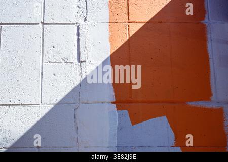Bright orange paint meets white concrete blocks. Sharp shadow slashes across the textured wall surface. Stock Photo