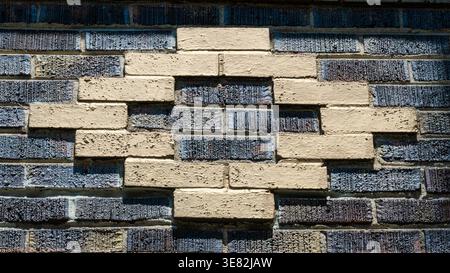 The brick wall features a striking geometric pattern. Dark and light bricks create a bold contrast. Texture contrasts add depth and visual interest. Stock Photo