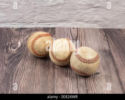 Three worn and dirty baseballs with red stitching arranged in a line on a dark wood grain surface Stock Photo