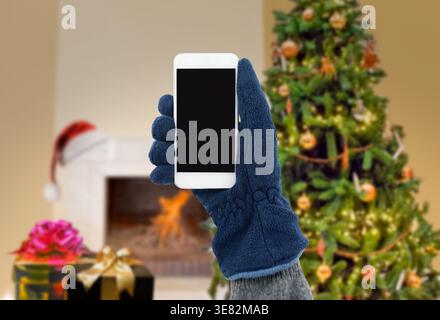 closeup of man with gloves using the smart phone with a Christmas tree background at home Stock Photo