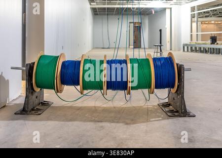 A photo of  cable caddy holds six spools of blue and green low-voltage cable on a construction site's concrete floor. Stock Photo