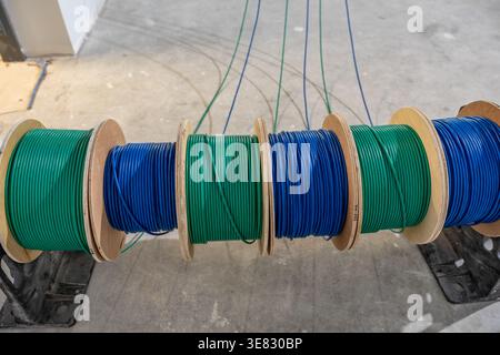 A photo of  cable caddy holds six spools of blue and green low-voltage cable on a construction site's concrete floor. Stock Photo