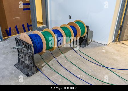 A photo of  cable caddy holds six spools of blue and green low-voltage cable on a construction site's concrete floor. Stock Photo