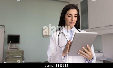 Doctor in white coat standing in examination room using tablet Stock Photo