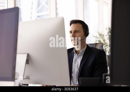Serious businessman in headset holding conversation via videocall on pc Stock Photo