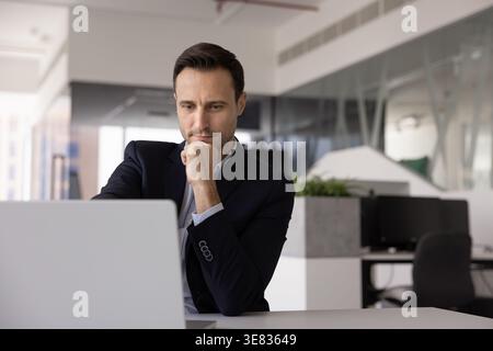 Confident Hispanic businessman planning project at office table by laptop Stock Photo