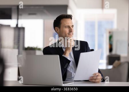 Focused Hispanic ceo using laptop printed documents at office desk Stock Photo