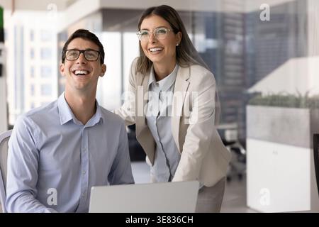 Young colleagues collaborating at laptop in contemporary skyscraper office Stock Photo
