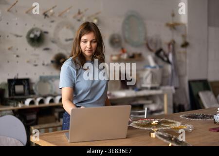 Caucasian female artisan using laptop in creative workshop studio Stock Photo