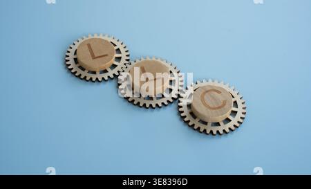 Business LLC letters on wooden gears representing limited liability company structure and mechanical operations on a blue background. Stock Photo