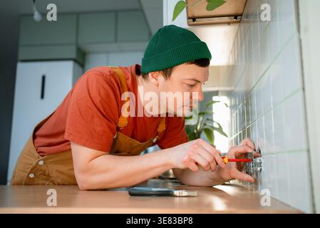 Electrician carefully installing a new electrical outlet on a white tiled kitchen backsplash, adding or replacing a power point during home renovation and repair work Stock Photo