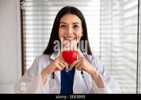 Headshot portrait of smiling female doctor holding red heart Stock Photo