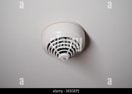 Smoke detector installed on ceiling in indoor space Stock Photo